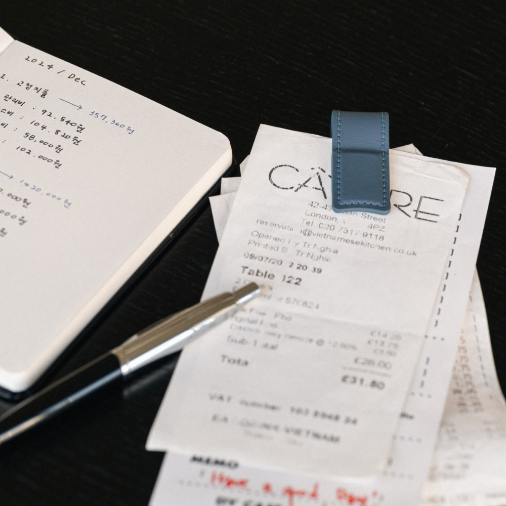 Labovarde Book Clip in Pale-Blue — Close-up view of the clip holding receipts next to an open notebook