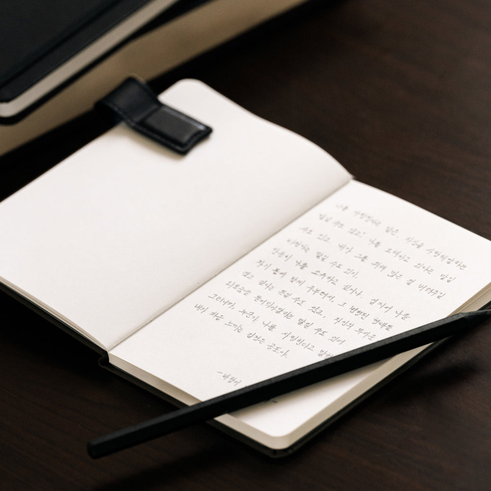 Labovarde Book Clip in Black — Close-up view of the clip on an open notebook with handwriting and a pencil