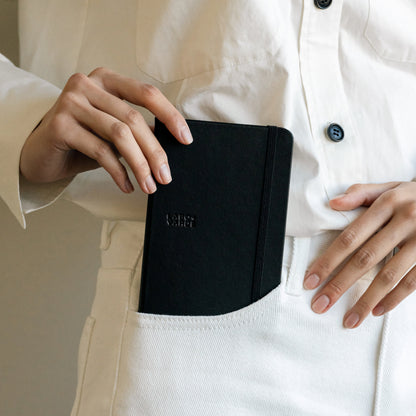 Labovarde Handy Note in Black — Close-up view of a hand putting the note into a white pants pocket